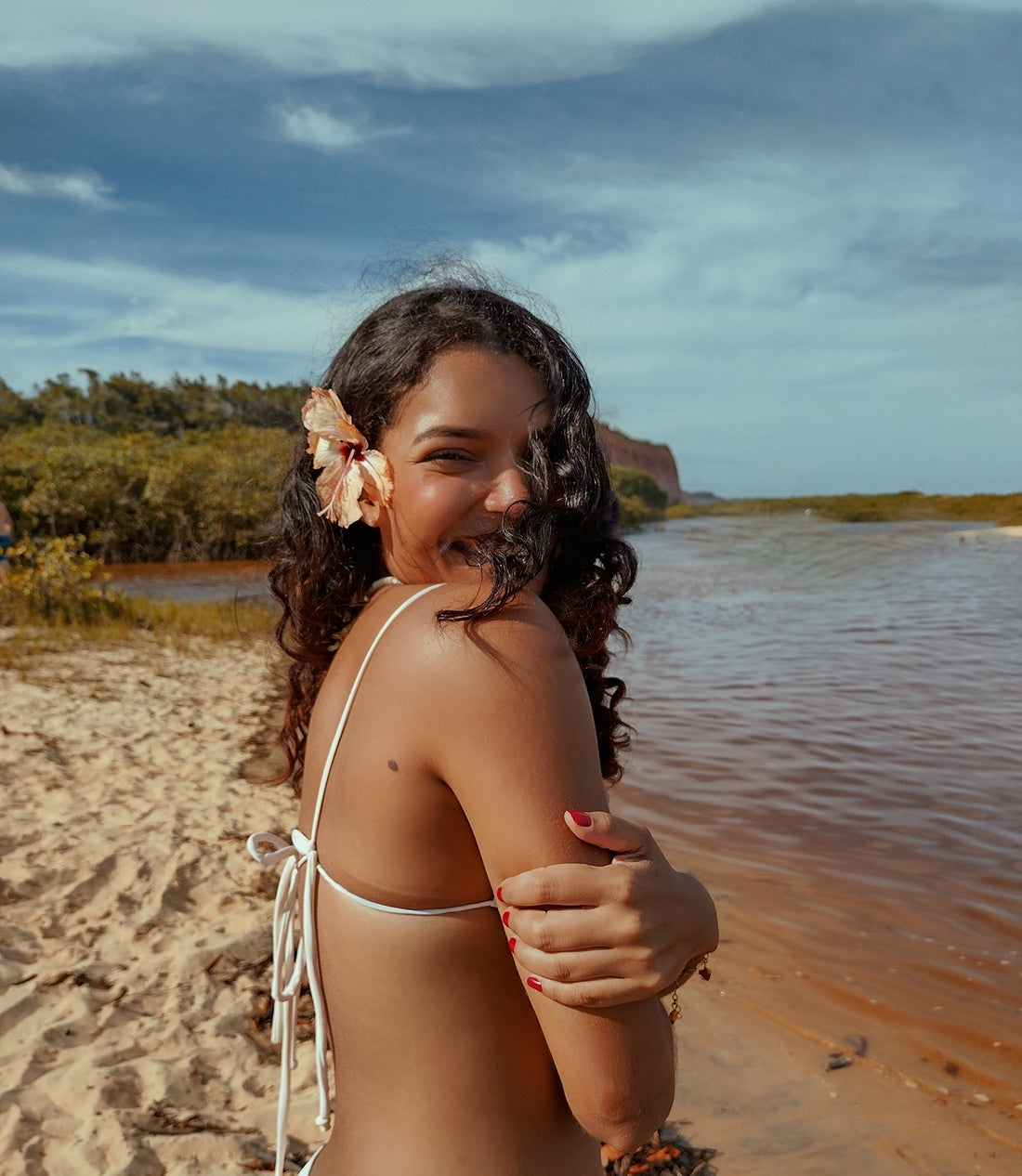 Mulher sorrindo na praia com flor no cabelo