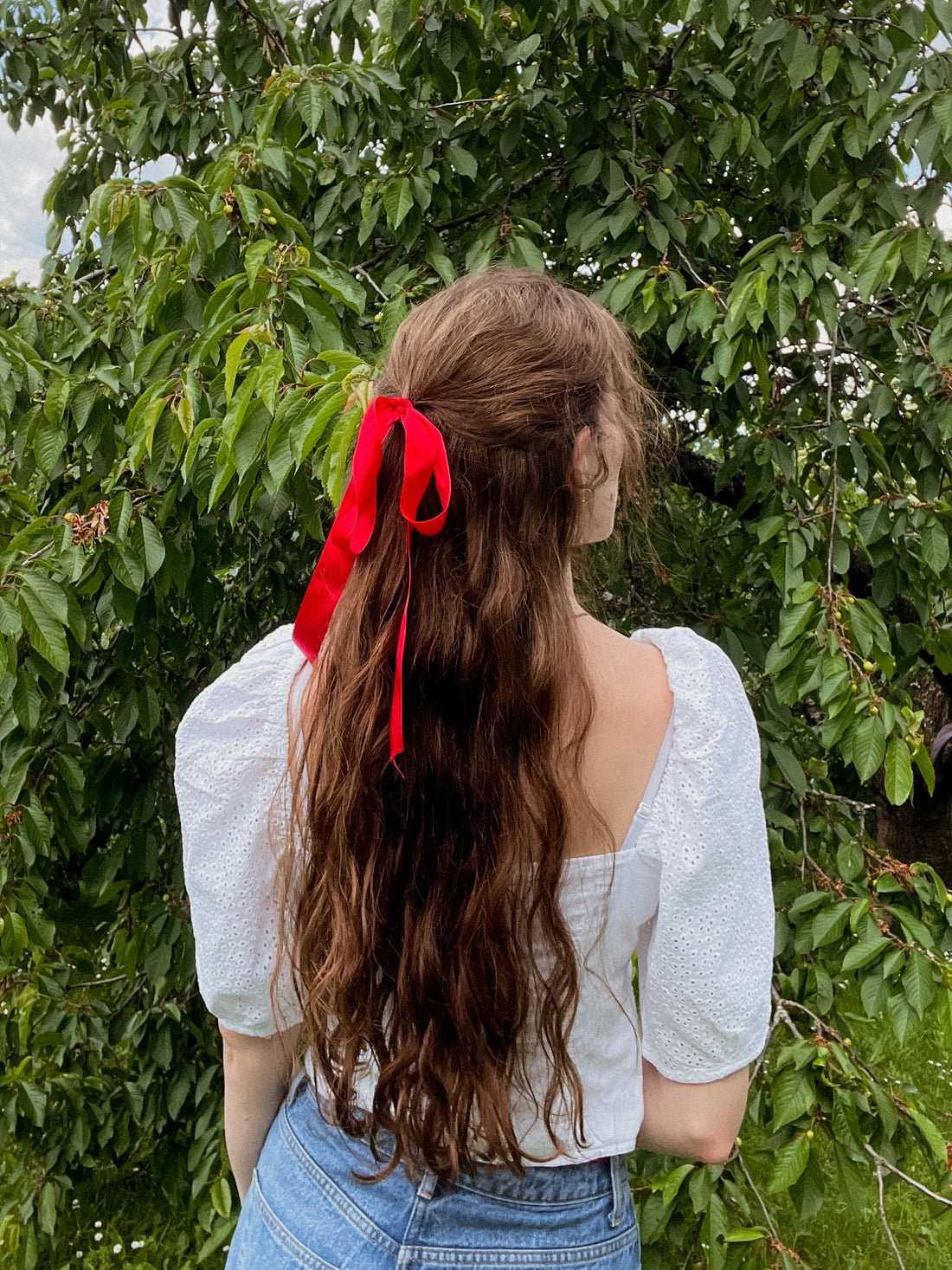 Mulher de cabelo longo com laço vermelho num jardim