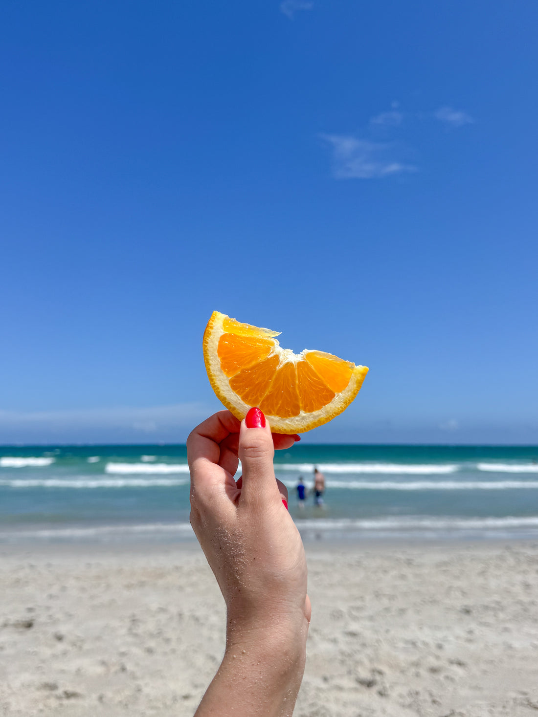 Mão segurando uma fatia de laranja na praia