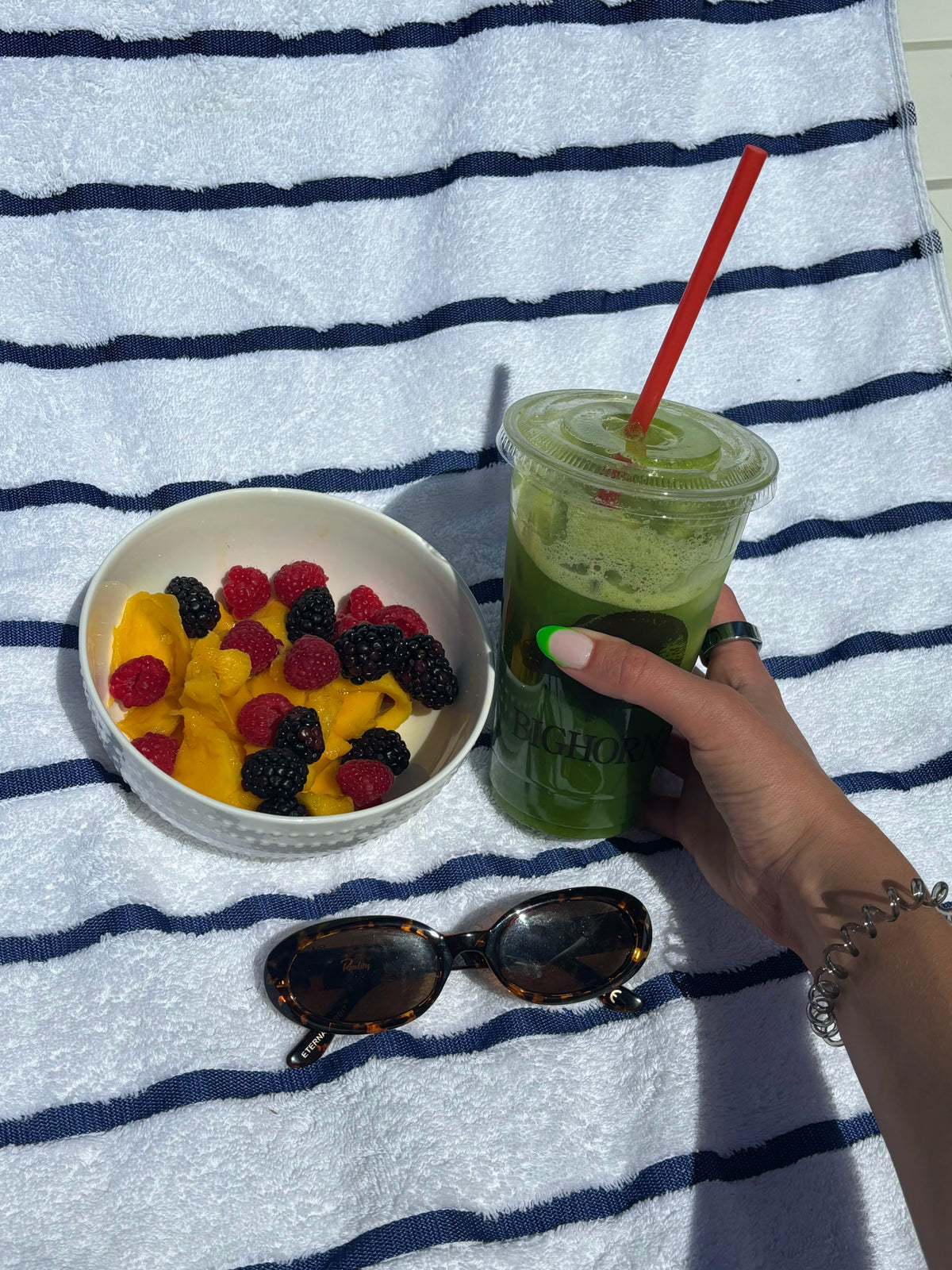 Suco verde e frutas sobre toalha listrada ao sol