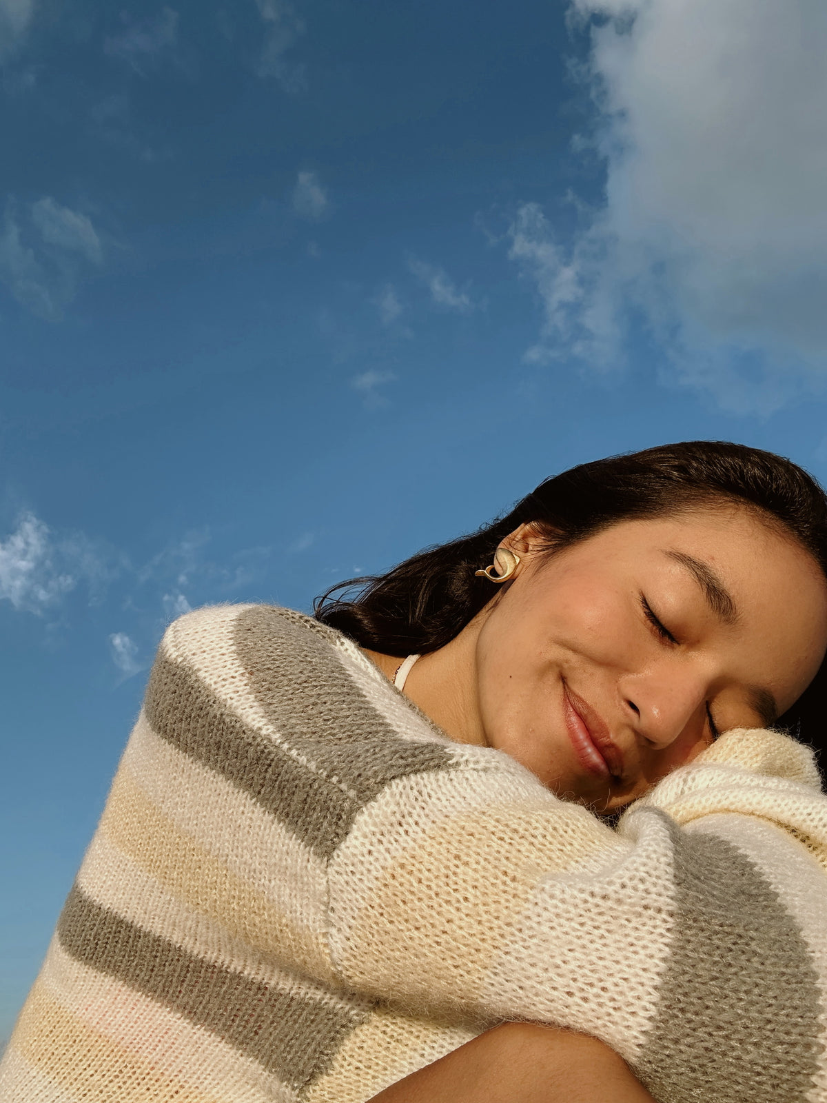 Mulher sorrindo de olhos fechados sob o céu azul