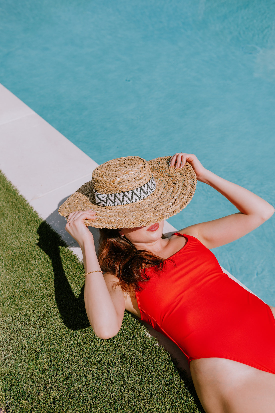 Mulher de maiô vermelho e chapéu de palha à beira da piscina
